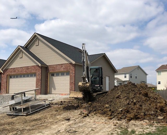 An excavator digging dirt in front of a new residential house.